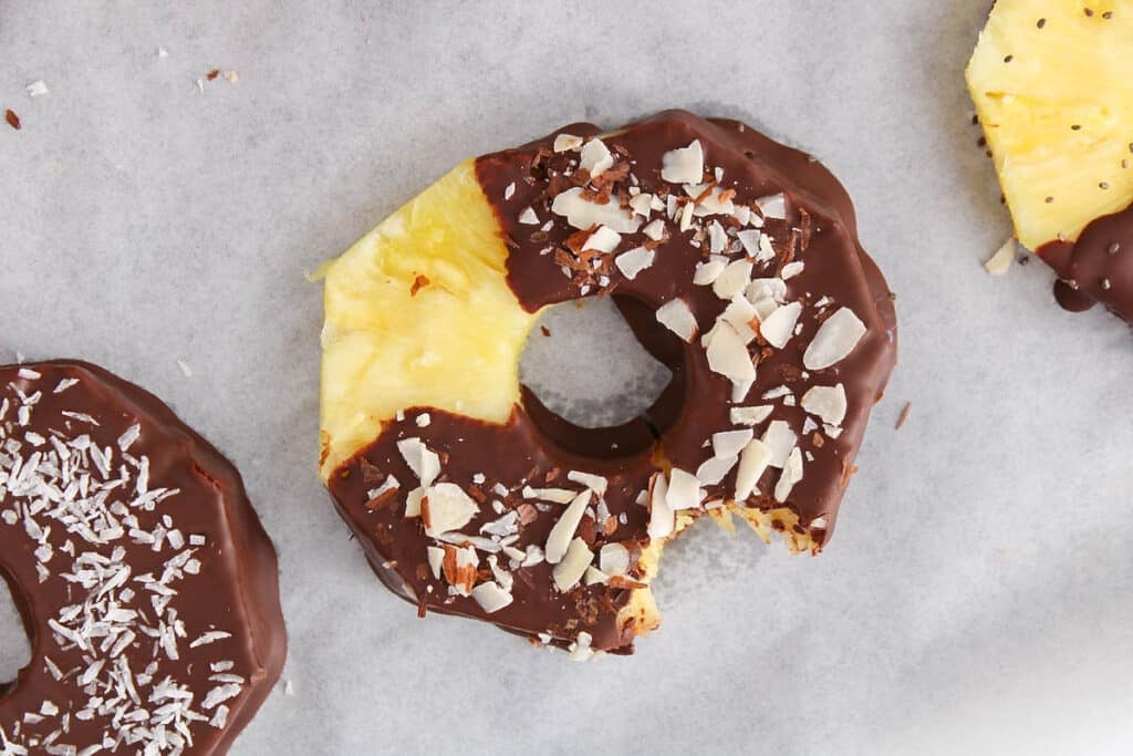 View on a chocolate covered pineapple garnished with slivered almonds on parchment paper.