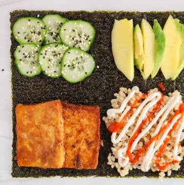 View on a sheet of nori filled with marinated tofu, cucumber, rice, avocado and mango to make a nori wrap.
