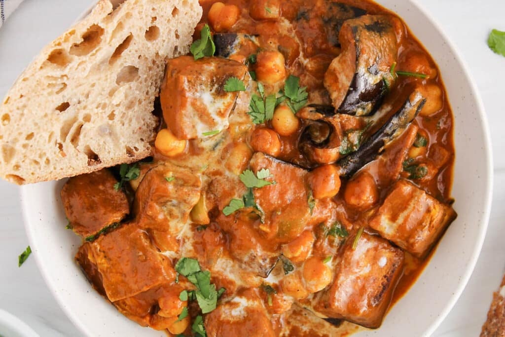 Close up on a bowl of creamy tikka masala sauce with roasted eggplant and chickpeas.