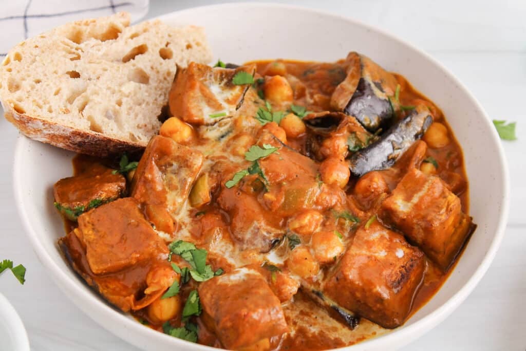 View on a bowl of vegan tikka masala made with eggplant ands chickpea with a side of bread.