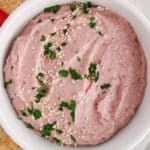 Close up on a bowl of homemade kidney bean hummus topped with sesame seeds and parsley.