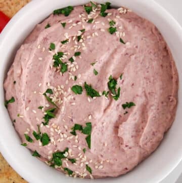 Close up on a bowl of homemade kidney bean hummus topped with sesame seeds and parsley.