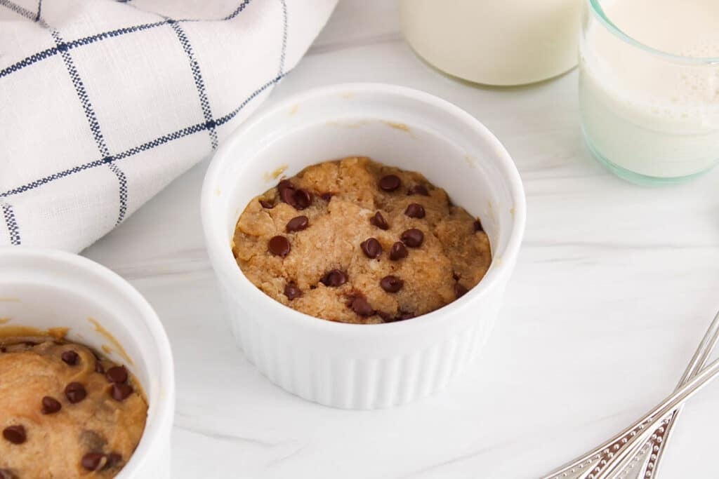 Front view on 2 vegan chocolate chip cookies in a mug with glasses of milk in the background.