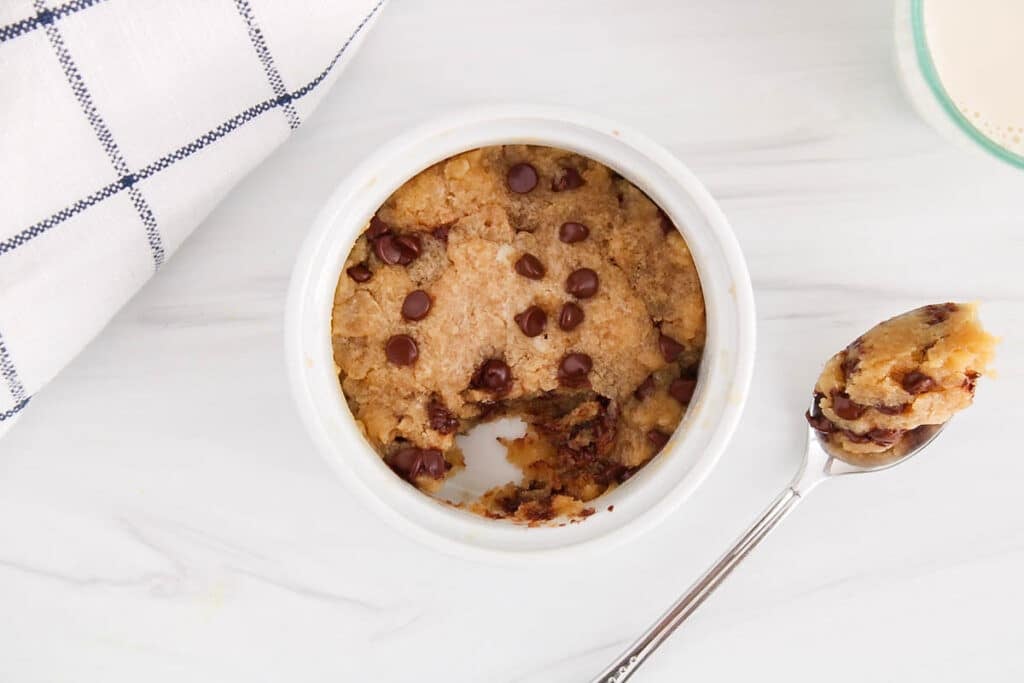 There is a vegan microwave chocolate chips cookie in a mug with a bite taken off.