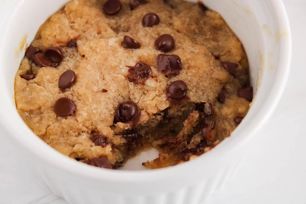 View on a vegan chocolate chip cookie with a bite taken off in a mug showing the texture in the middle.