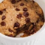 View on a vegan chocolate chip cookie with a bite taken off in a mug showing the texture in the middle.