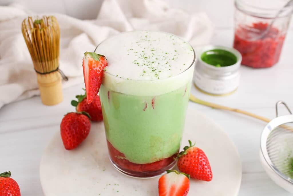 View on an iced strawberry matcha oat latte showing the bright green, white foam and red strawberry layers.