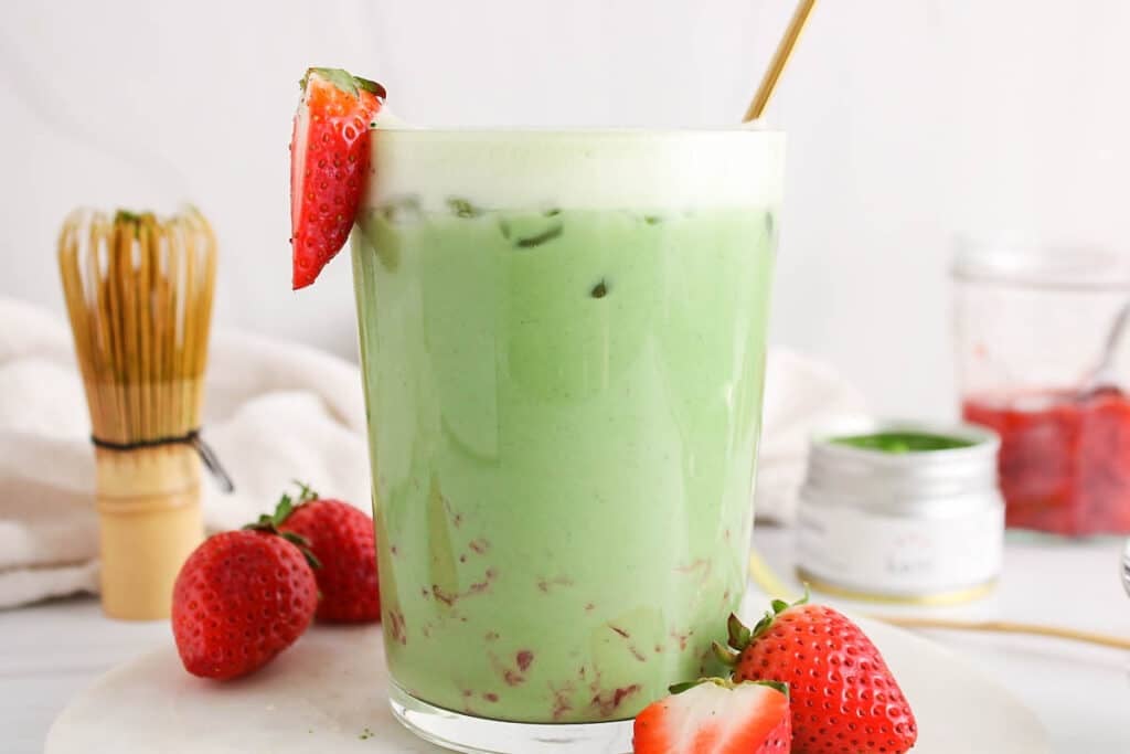 View on a bright green matcha oat latte with pieces of strawberries.