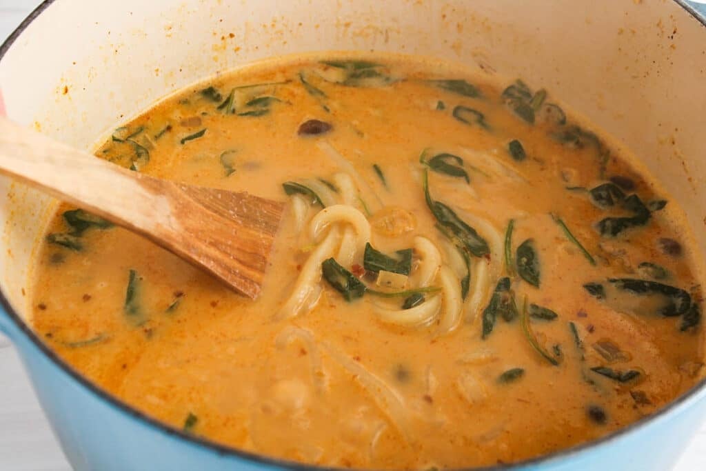 Showing a large pot of udon in a red curry broth.