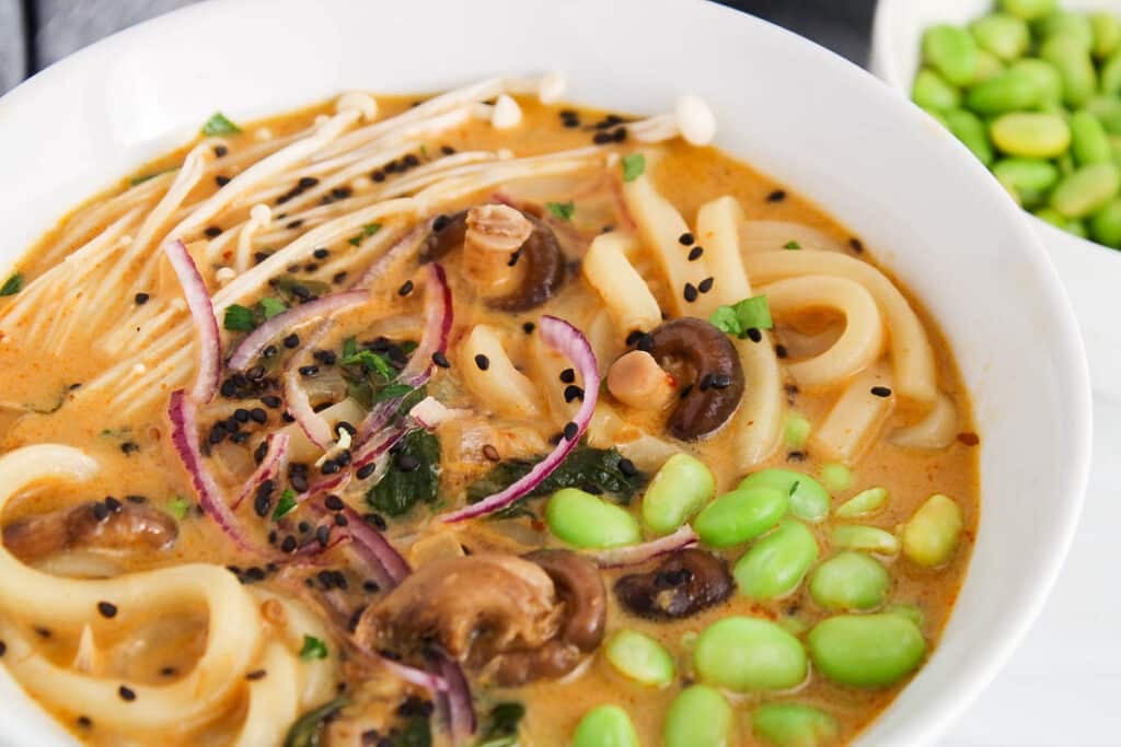 Close up on the topping ingredients of a red curry udon noodle soup.