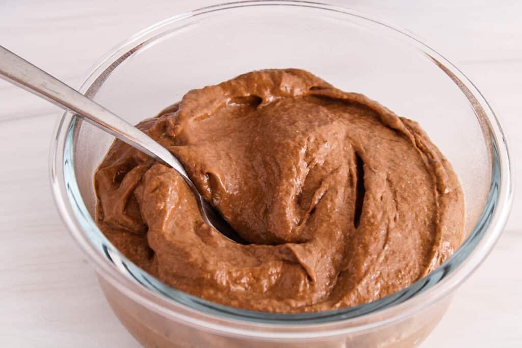 Close up on a dairy-free avocado chia chocolate pudding in a bowl with a spoon stirring.