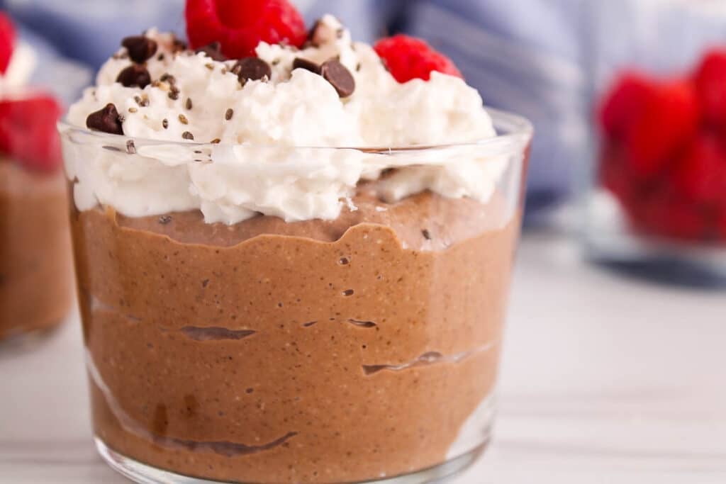 Close up on a creamy avocado chia chocolate pudding in a cup topped with whipped cream.