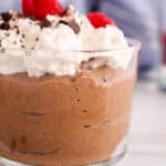 Close up on a creamy avocado chia chocolate pudding in a cup topped with whipped cream.