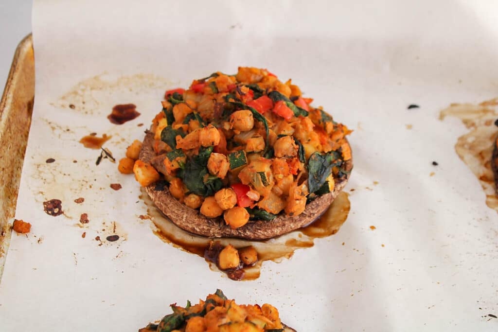 Close up on a oven-baked portobello mushroom on a baking sheet and stuffed with chickpeas and lots of vegetables.