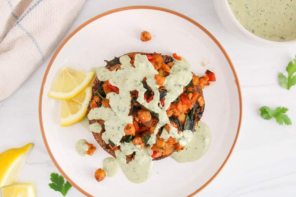 Overhead view on a vegetable and chickpea stuffed portobello mushroom garnished with a tahini lemon herb sauce.