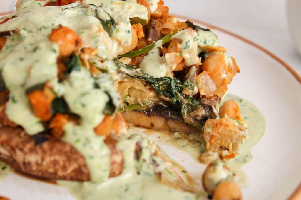 There is a bite taken off a vegan chickpea and veggie stuffed portobello mushroom.
