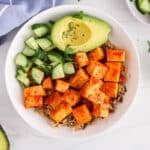 View on a vegan buddha bowl made with avocado and cucumber and featuring a saucy harissa tofu.