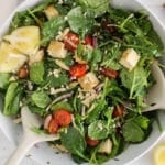 View on a large bowl of arugula spinach salad with vegan feta cheese, cherry tomatoes, red onion and nuts.