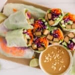 Plate filled with halved vegan tempeh spring rolls with a side of peanut butter sauce.