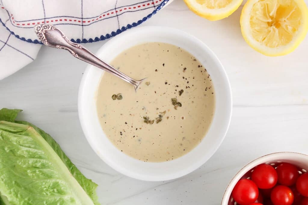 Vegan tahini Cesar dressing in a bowl garnished with capers and black pepper.
