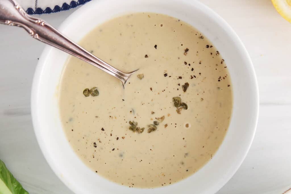 Vegan tahini Cesar dressing in a bowl garnished with capers and black pepper.