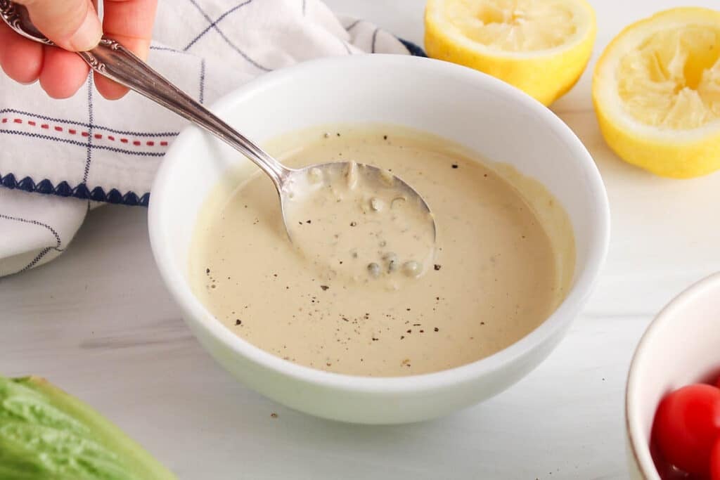 There is a spoon taking some plant-based tahini Cesar dressing from a bowl to show texture.