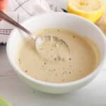 There is a spoon taking some plant-based tahini Cesar dressing from a bowl to show texture.