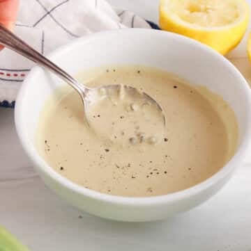 There is a spoon taking some plant-based tahini Cesar dressing from a bowl to show texture.