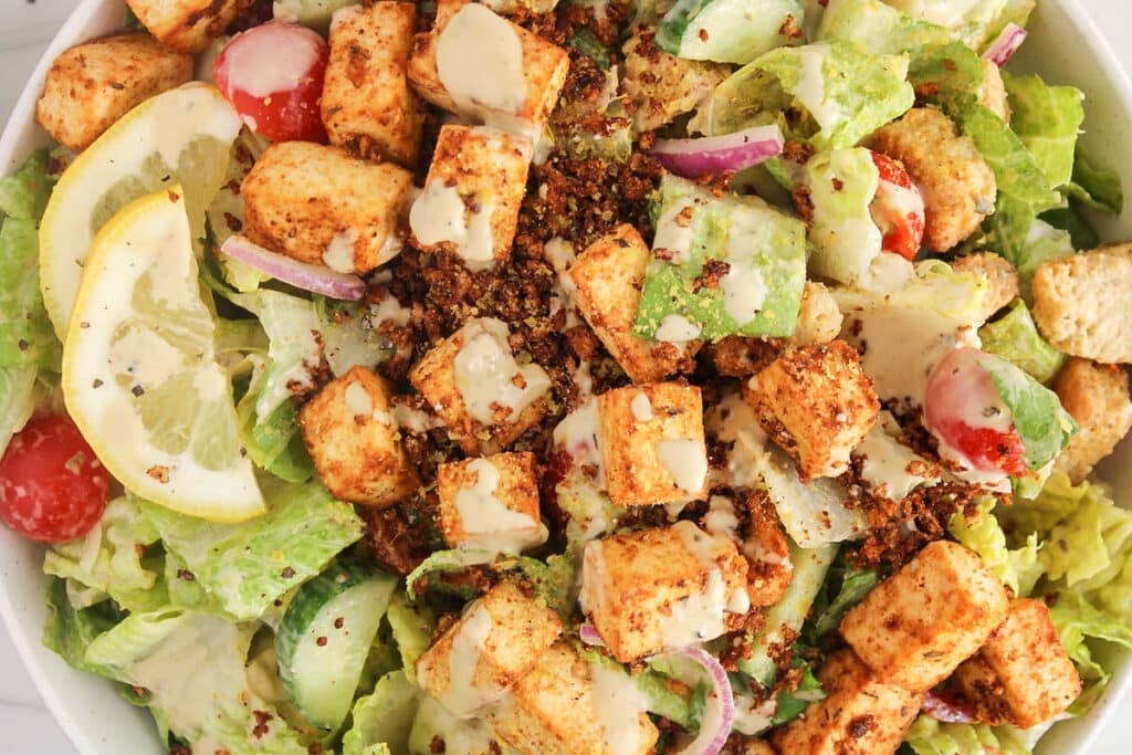 Bowl of plant-based salad with Vegan Caesar dressing, vegetables and Cajun seasoned tofu.