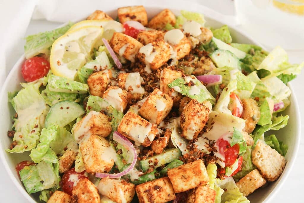 Large bowl of vegan Caesar salad topped with Cajun tofu.