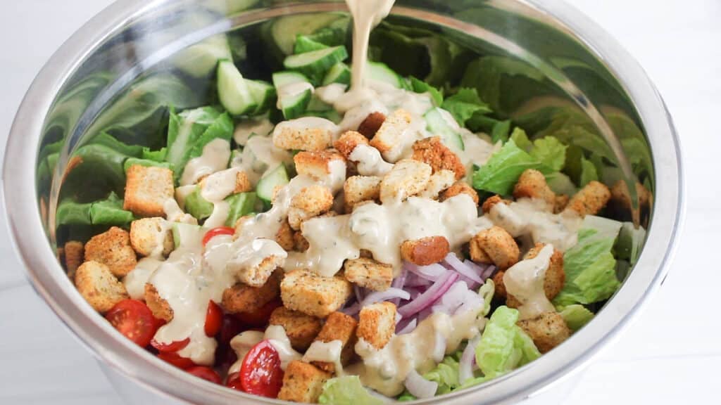 Pouring a vegan tahini Cesar dresing over a salad in a bowl.