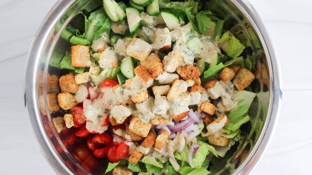 View on a large mixing bowl with salad, veggies, croutons and a drizzle of vegan Caesar dressing.