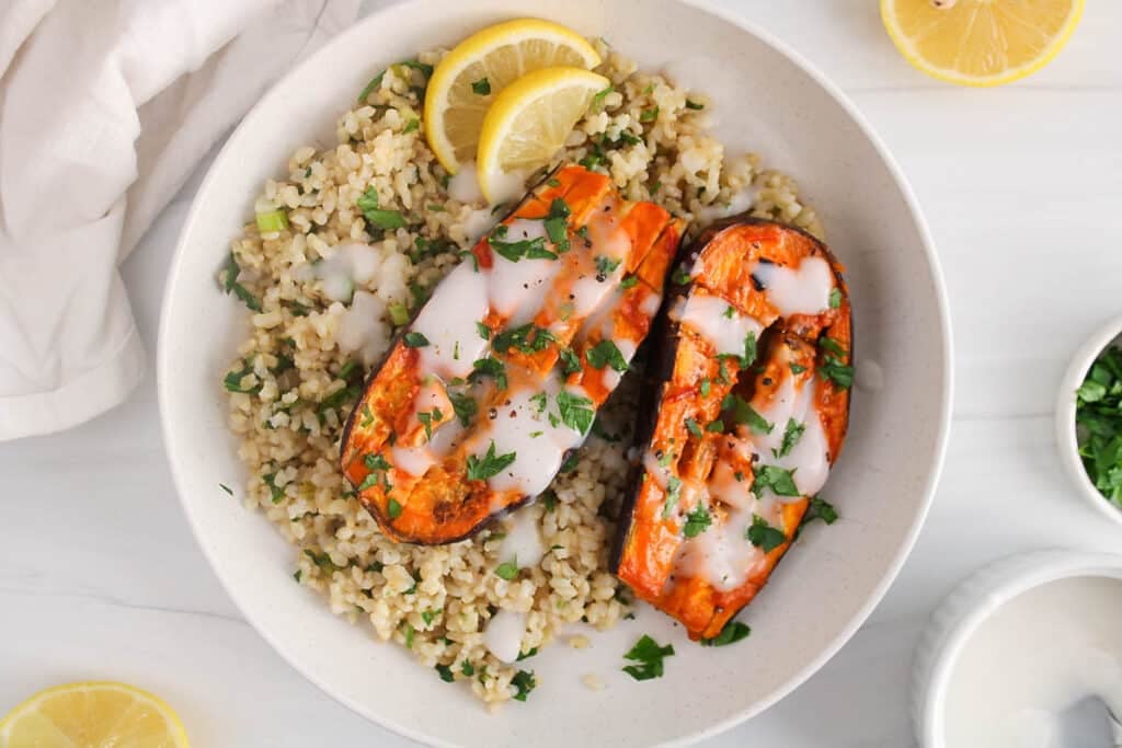Plate with herbed rice, oven-baked harissa aubergine and yogurt garlic sauce with a side of lemon wedges.