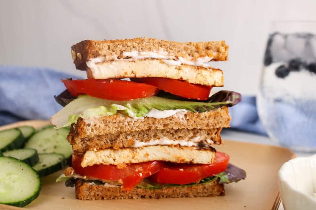 Two halves of vegan tofu BLT sandwich over each other on a plate.