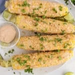 Recipe for vegan Elote showing 4 corn cobs with Mexican mayo and cilantro over a plate.