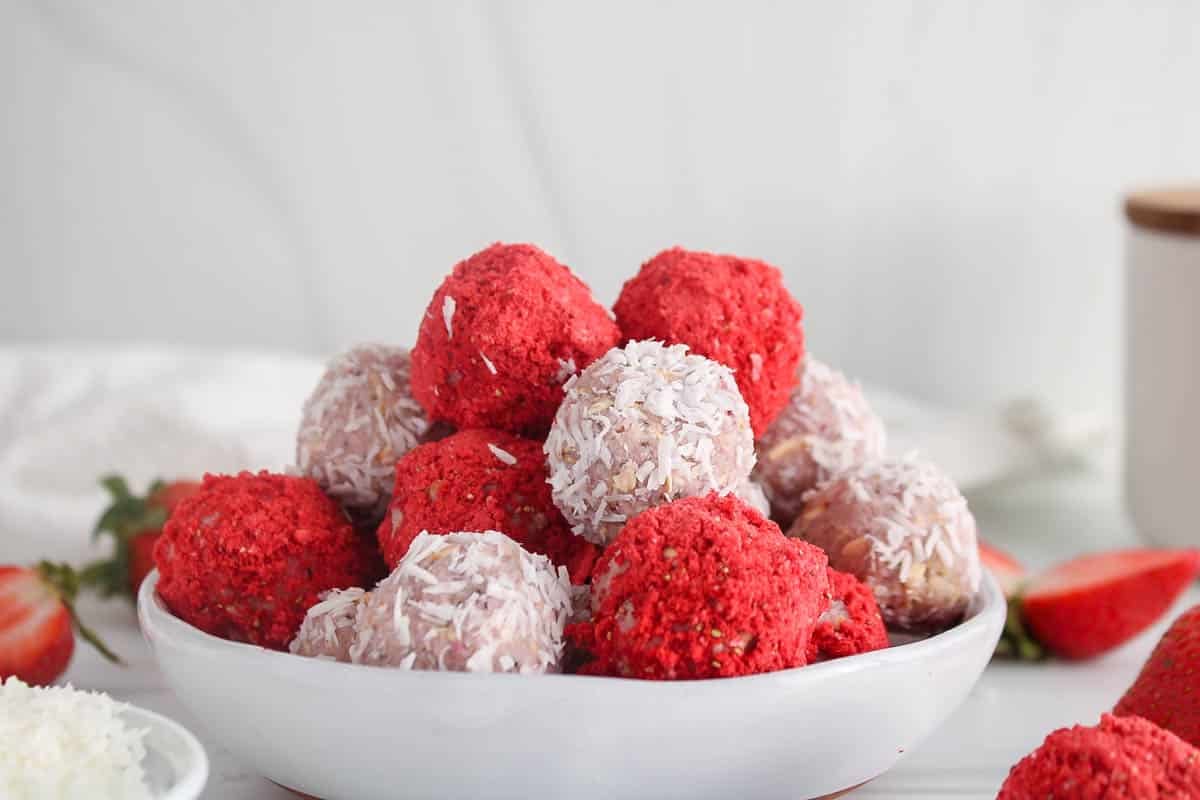 Coconut covered and freeze-dried strawberry covered healthy bliss balls on a small plate.