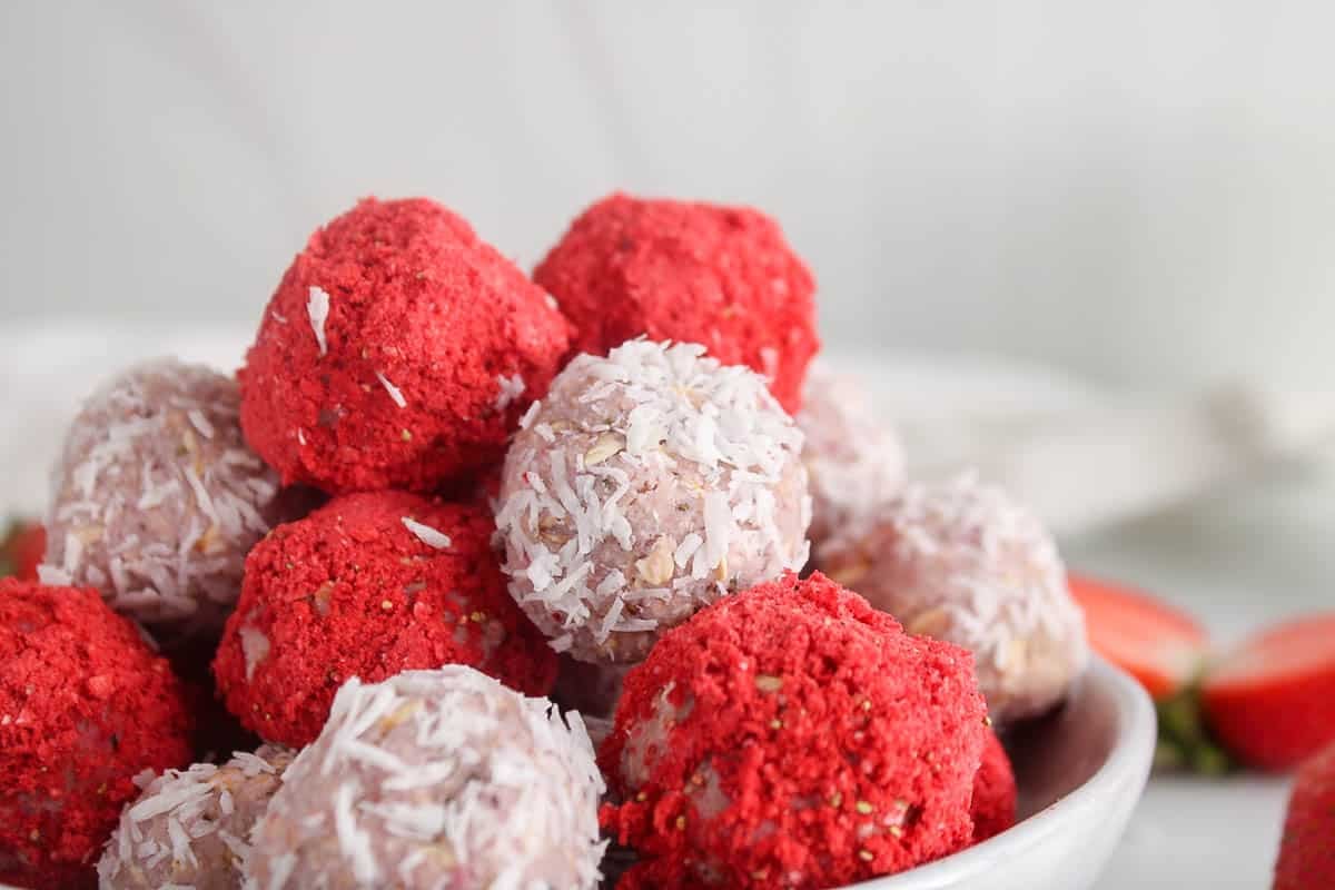 Pink vegan bliss ball made with fresh strawberries and covered with either freeze dried strawberries or desiccated coconut.
