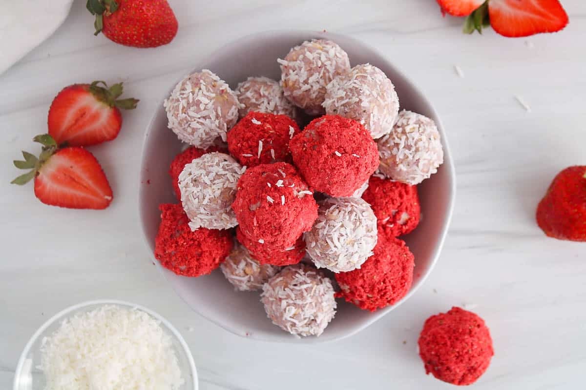 Table with fresh strawberries and a small plate filled with colorful strawberry bliss balls.