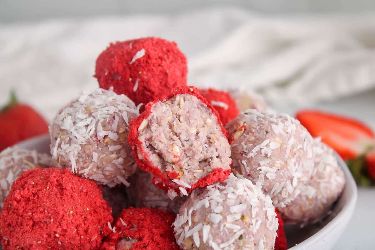Showing a vegan strawberry bliss ball with a bite taken off to show the middle texture.