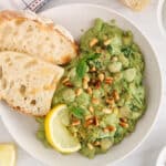 Bowl filled with a creamy vegan pesto butter beans stew with a side of bread and lemon.