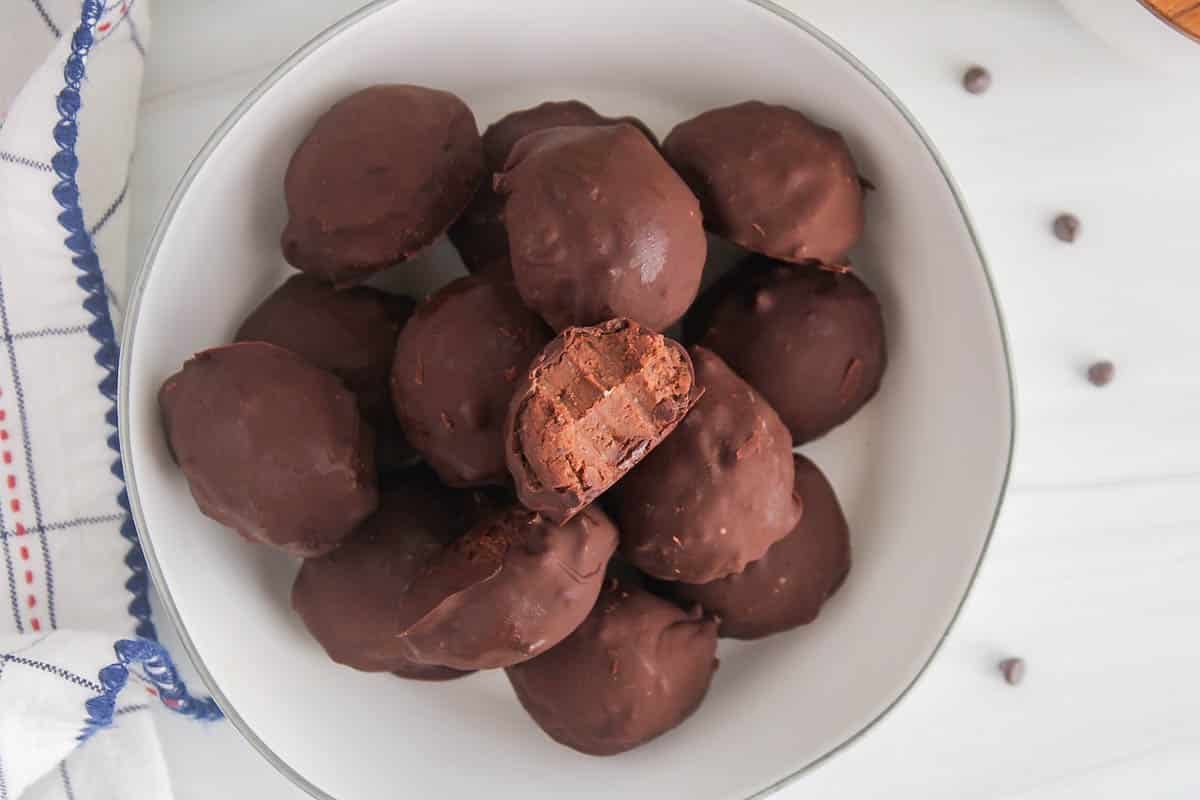 A dozen of vegan chickpea truffles in a white bowl with the top one that has a bite taken off to show the middle.