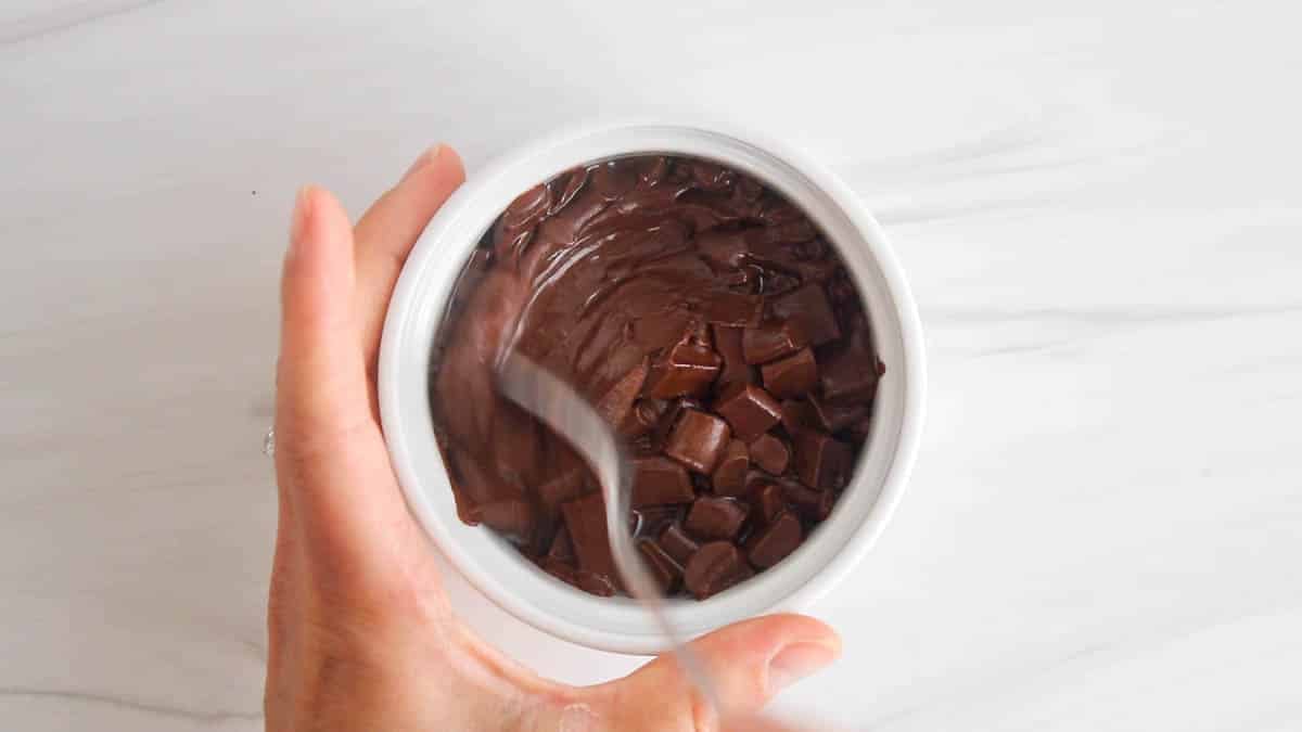 Melted chocolate in a white bowl with a spoon stirring.