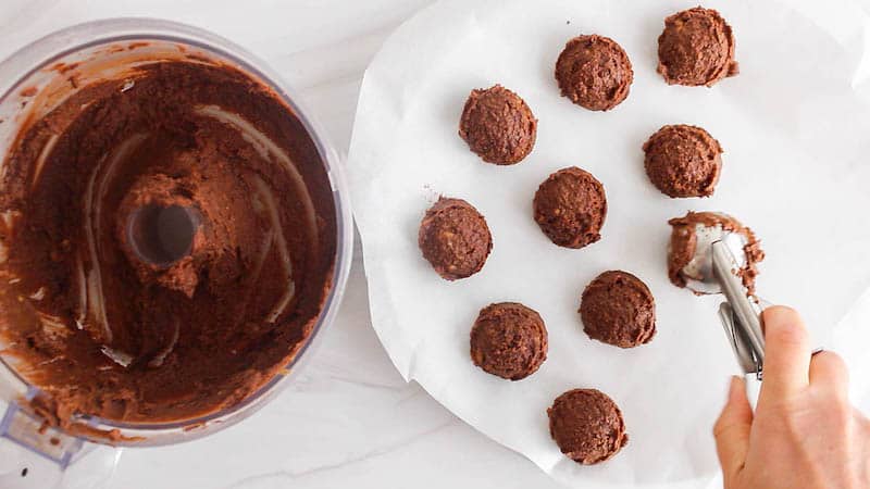 Ice cream scoop scooping the truffle batter over parchment paper.