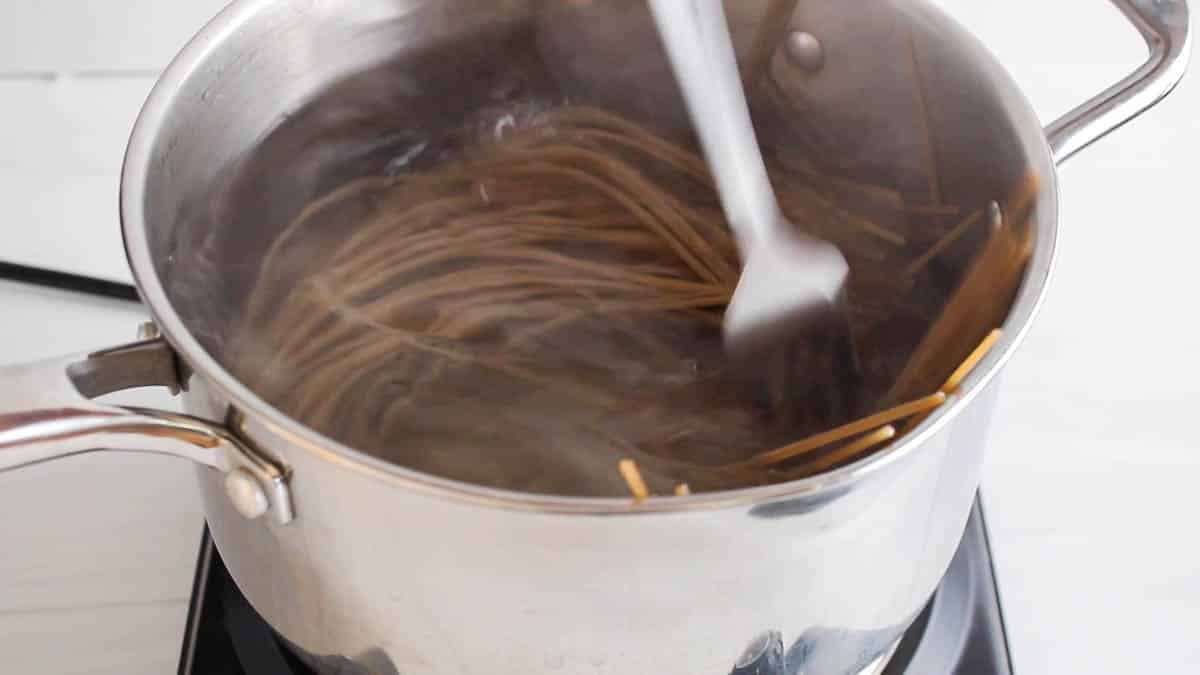 A medium pot with simmering noodles in water.