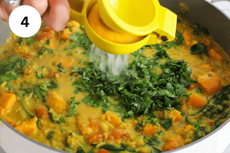 Adding spinach, cilantro and lemon juice to a pan with a curry stew.