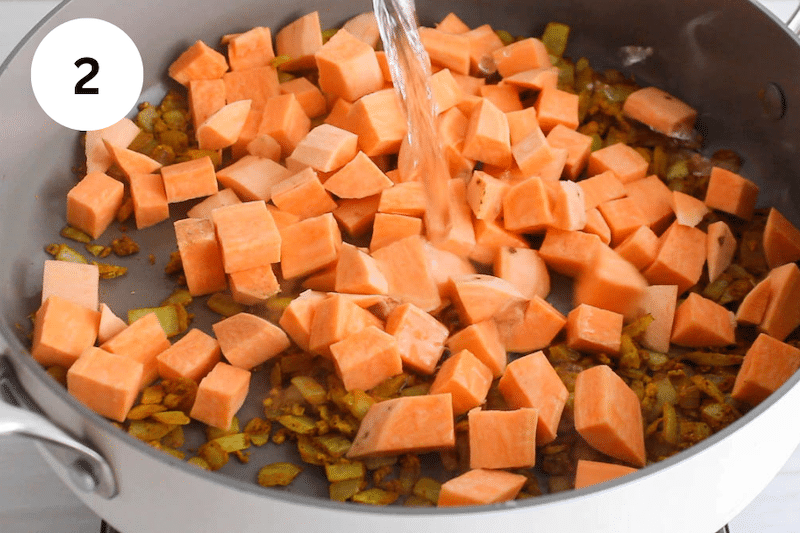 Adding sweet potatoes and water to a pan with vegetables.