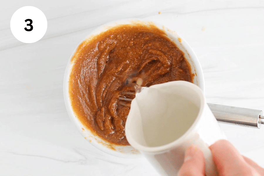 A small white jar pouring water in a peanut butter thick mixture.