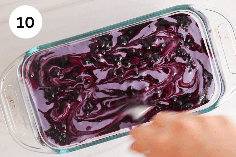 A spoon swirling blueberries in homemade ice cream.