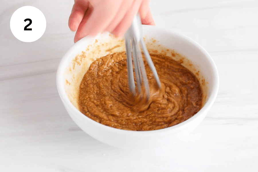 A small whisk stirring a peanut butter mixture.