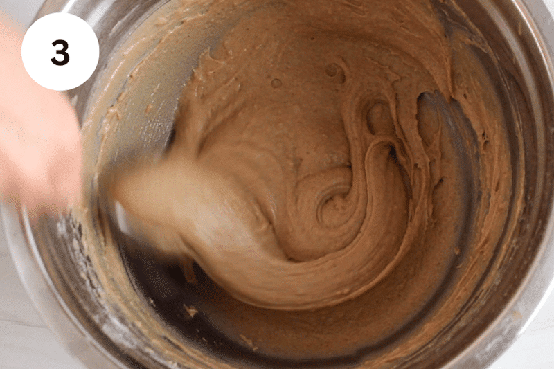 A large spoon stirring a muffin batter in a large bowl.